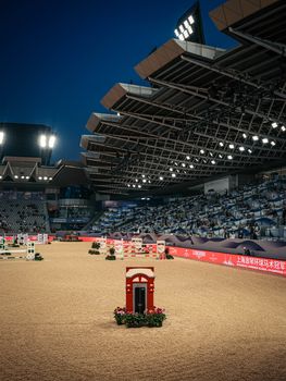 A well-lit indoor horse arena ready for competition under a night sky.