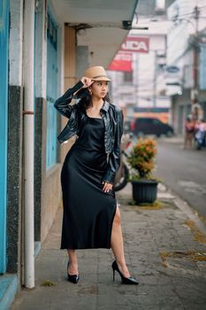 Stylish woman in black dress and hat posing on a street in Bandung, Indonesia.