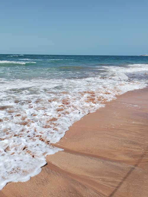 Free Serene view of waves gently washing over a sandy beach under a clear blue sky. Stock Photo