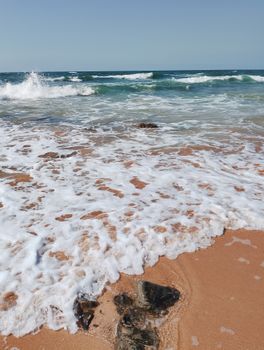 Gentle waves lapping a sandy beach on a clear summer day, evoking tranquility and escape.