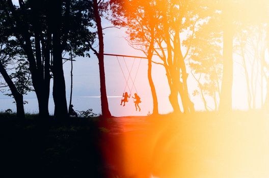 Silhouetted children on a swing in a forest at sunset by the Baltic Sea.