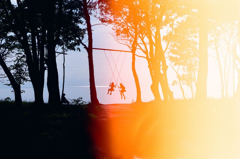 Silhouetted children on a swing in a forest at sunset by the Baltic Sea.