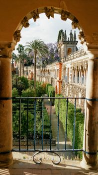 View through an arched window of the gardens and architecture of Alcázar in Seville, Spain.
