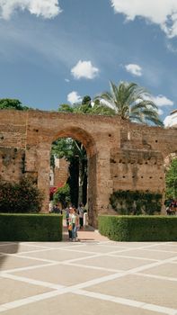 Tourists exploring the historic Alcázar of Seville, Spain, with clear summer skies.