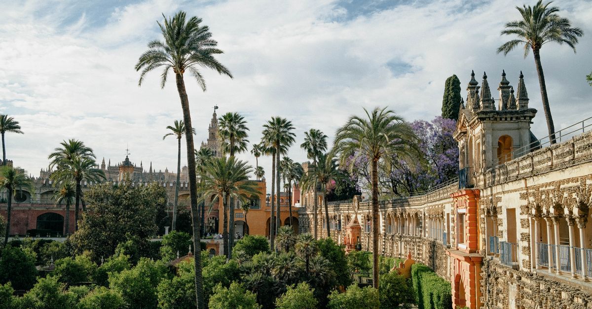 Lush gardens of Real Alcázar, Seville with palm trees and architectural details under a bright sky.