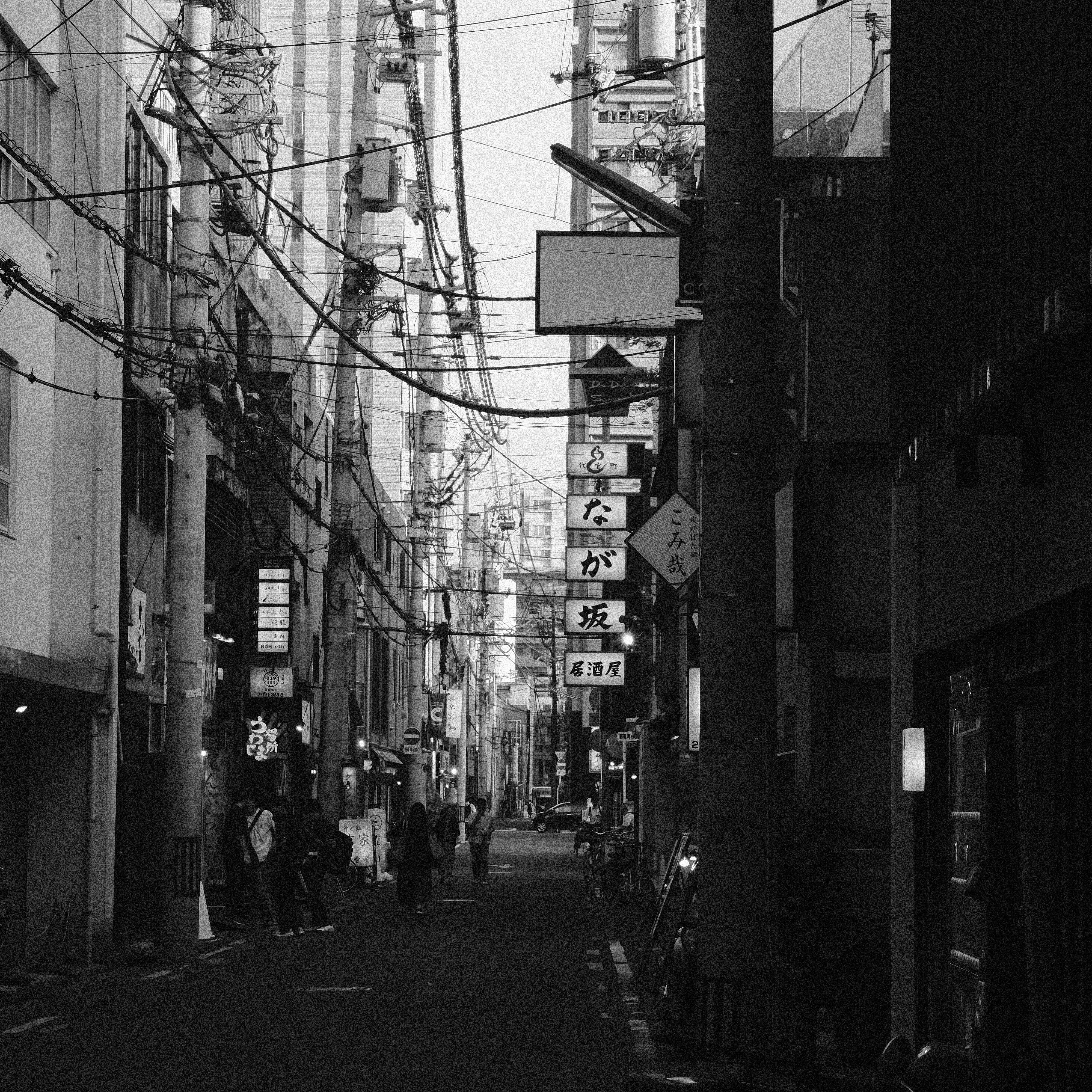 A narrow street in Japan with urban architecture and overhead wires in black and white.