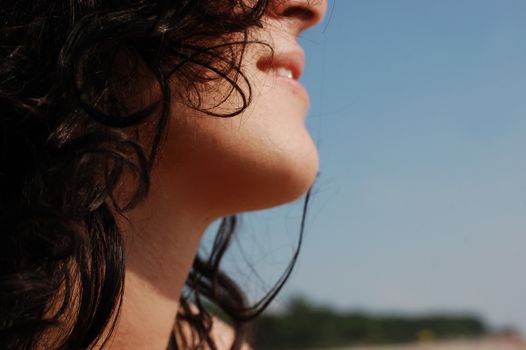 Close-up profile of a woman with curly hair enjoying a sunny day outdoors.