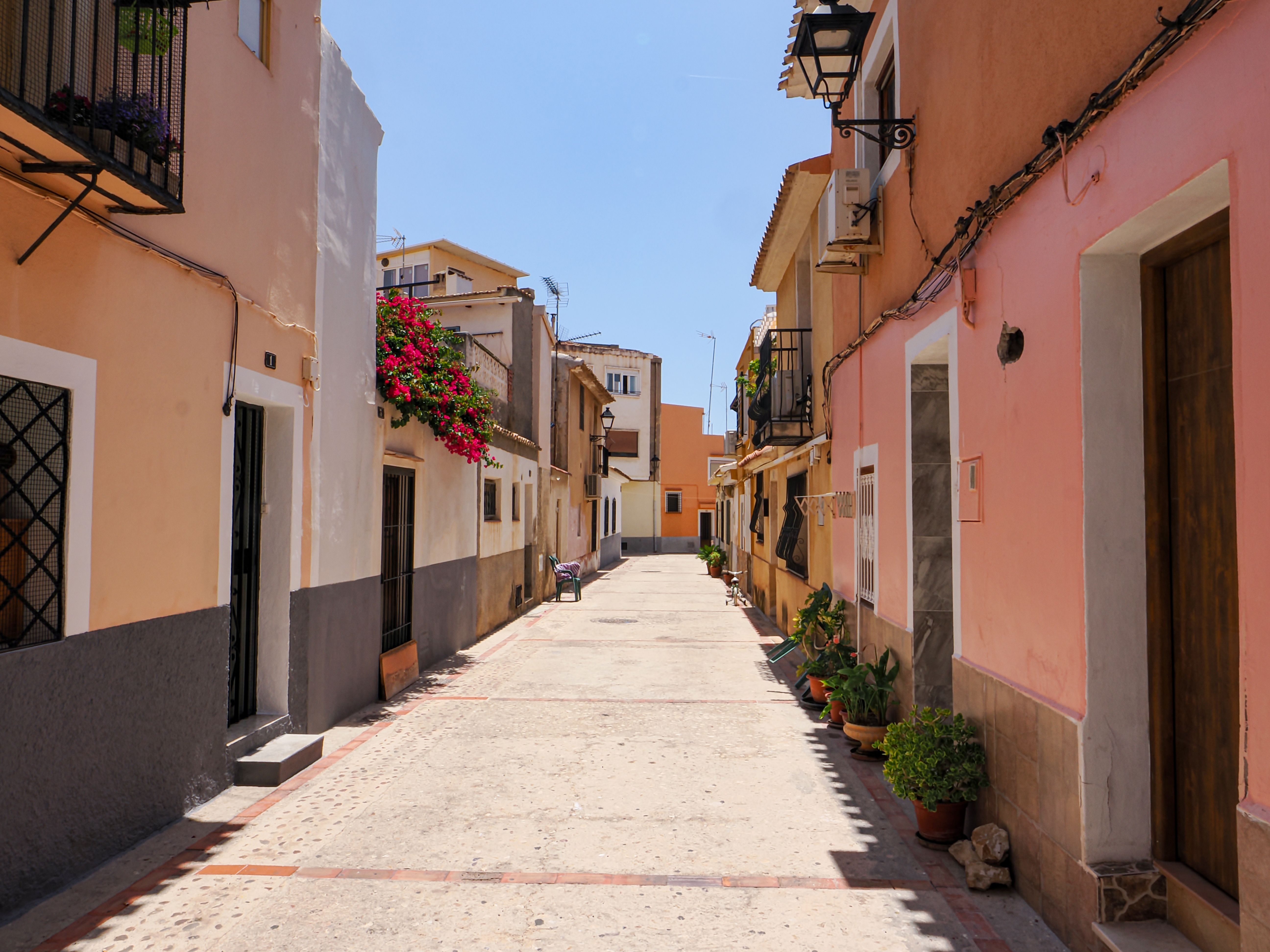 A vibrant alley in Alicante with colorful facades and summer blooms, capturing Spanish charm.