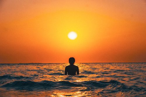 Free A silhouette of an individual wading in the ocean during a vibrant sunset in Makassar, Indonesia. Stock Photo