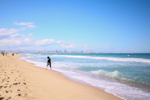 Free A peaceful beach scene with people walking along the shoreline under a clear blue sky. Stock Photo