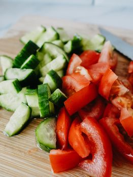 Sliced cucumbers and tomatoes on a wooden cutting board, ideal for a fresh salad.