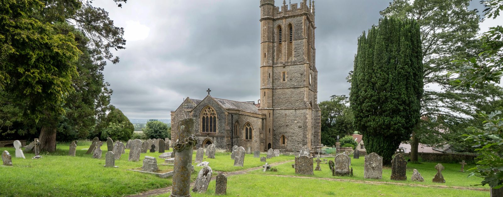 A picturesque English church and graveyard under a cloudy sky in Stalbridge, UK, showcasing stone architecture.