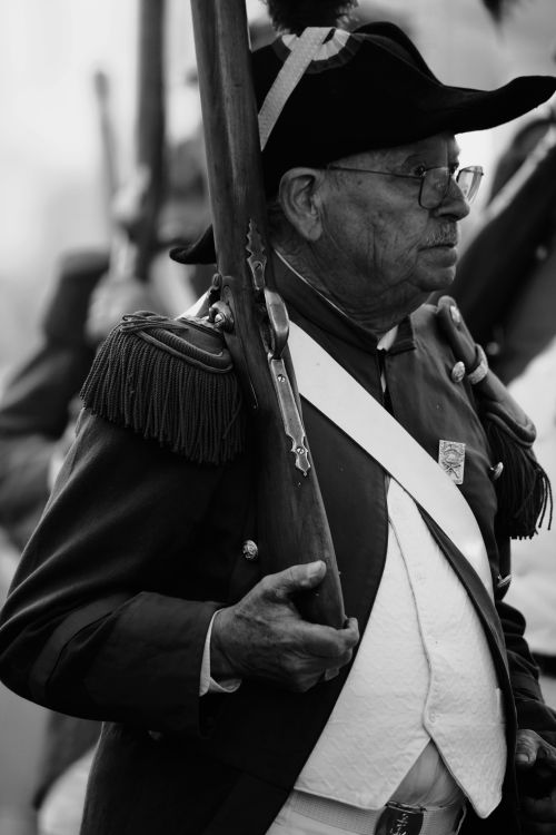 Free An aged reenactor in historic military uniform holds a rifle during a reenactment. Stock Photo