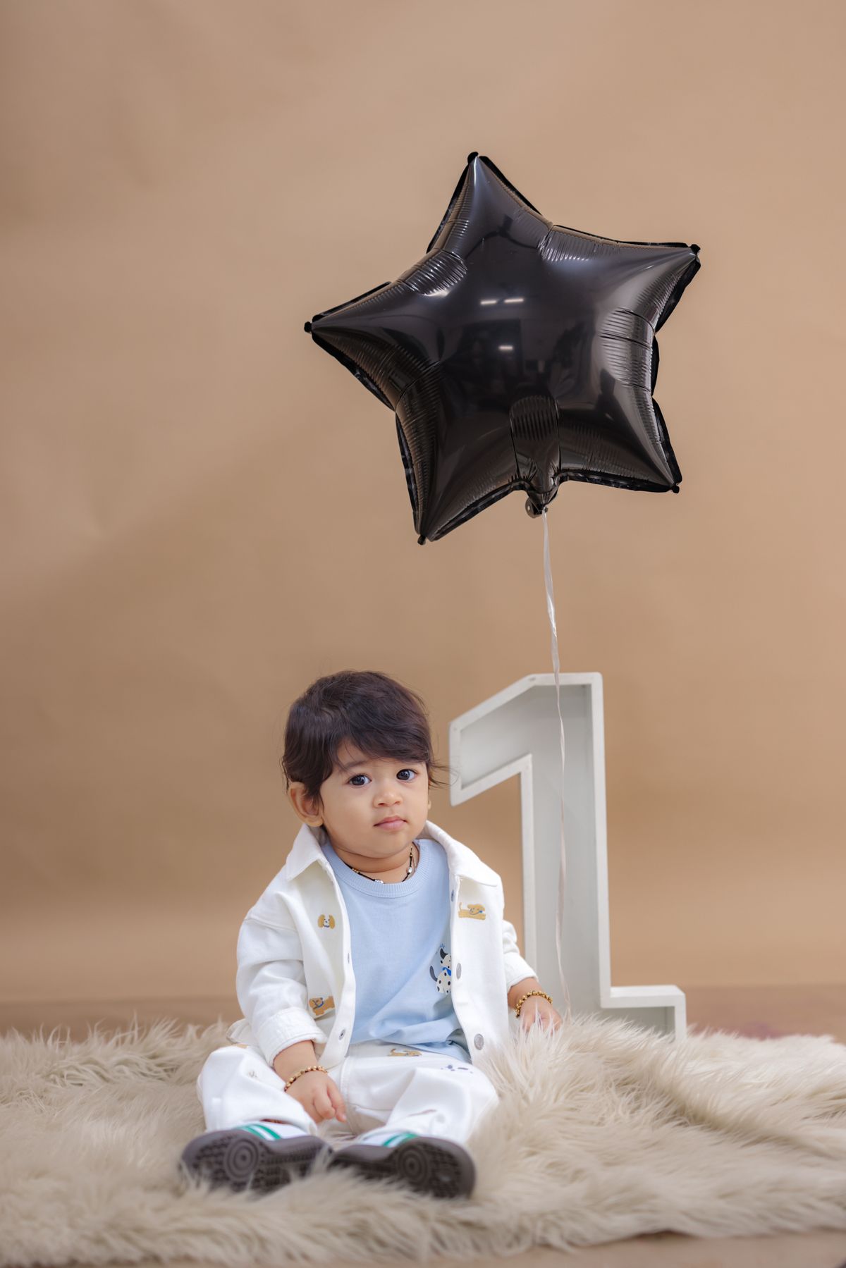 A baby boy celebrates his first birthday with a star balloon and number one prop. Stock Photo.
