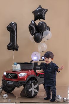 A toddler celebrating their first birthday with balloons and a toy car.