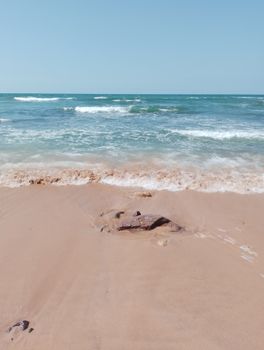 Peaceful sandy beach with gentle waves under a clear blue sky.