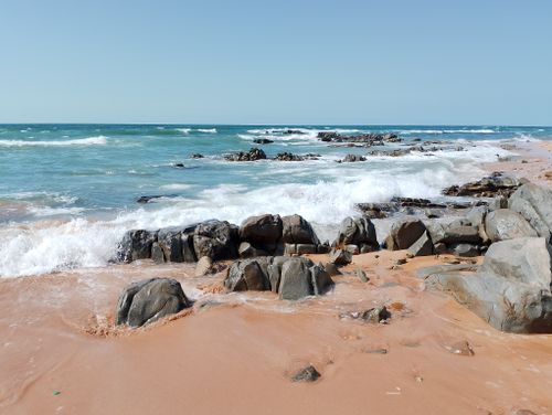 Free A vibrant beach scene with crashing waves and rocky shoreline under a clear blue sky. Stock Photo