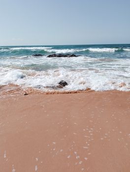 Tranquil ocean waves gently crashing on a peaceful sandy beach under clear blue skies.