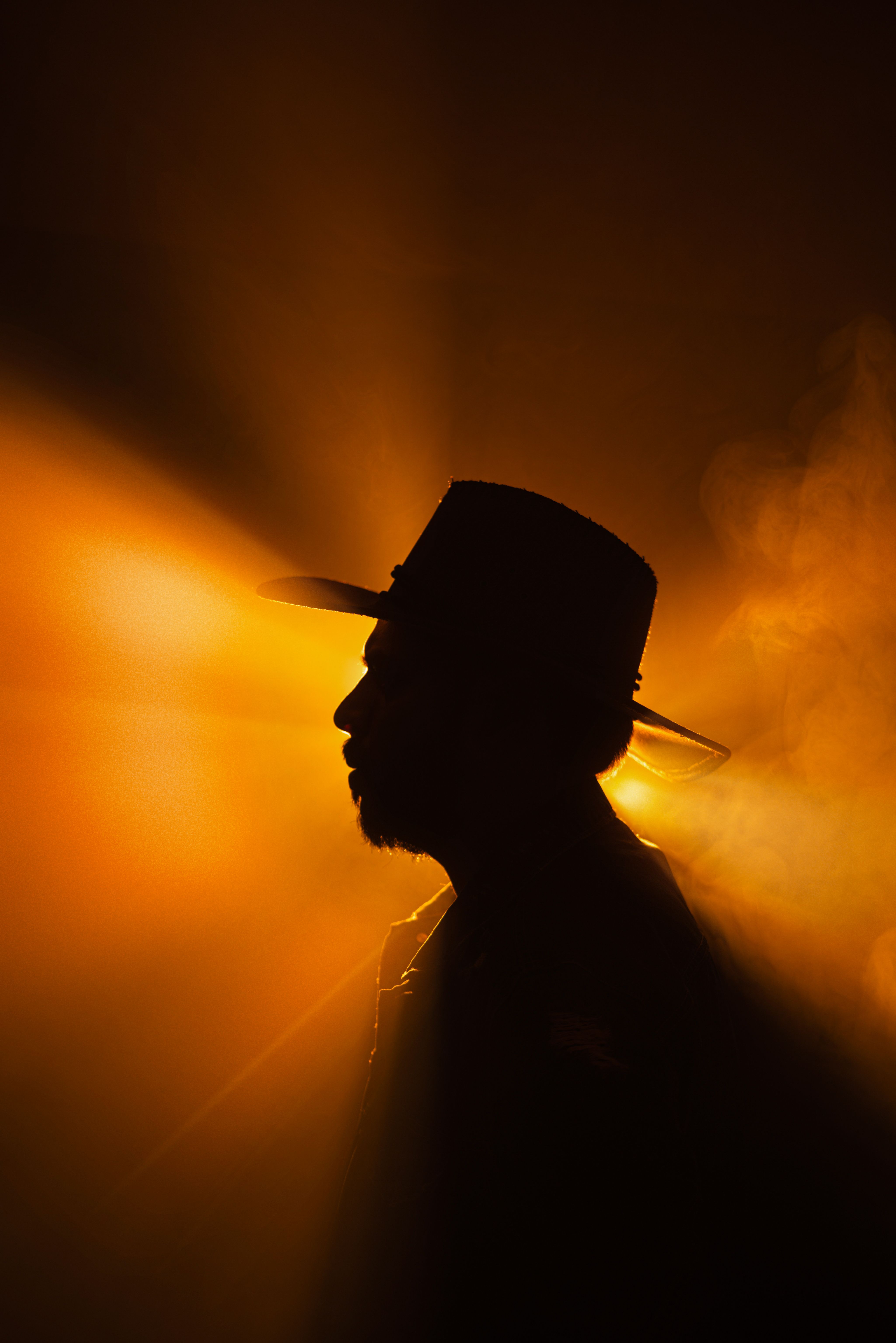 Artistic silhouette of a man wearing a hat, dramatically backlit with warm orange light.