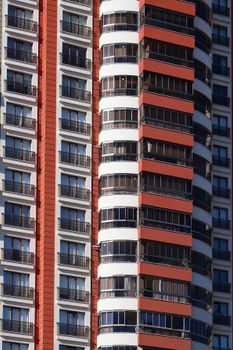 A detailed view of a contemporary high-rise building showcasing red and white facade with numerous balconies.
