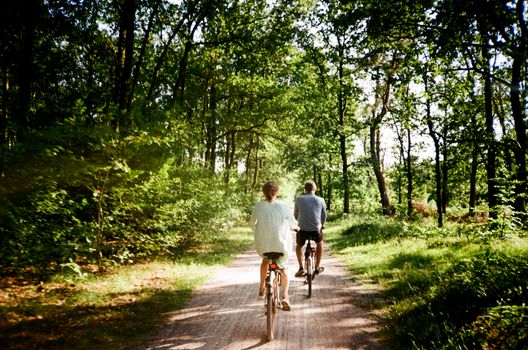 Two people biking on a forest trail under sunny skies, summer vibes.