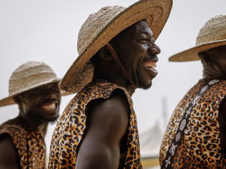 Smiling African men in straw hats and traditional leopard print attire, creating a lively and joyful atmosphere.
