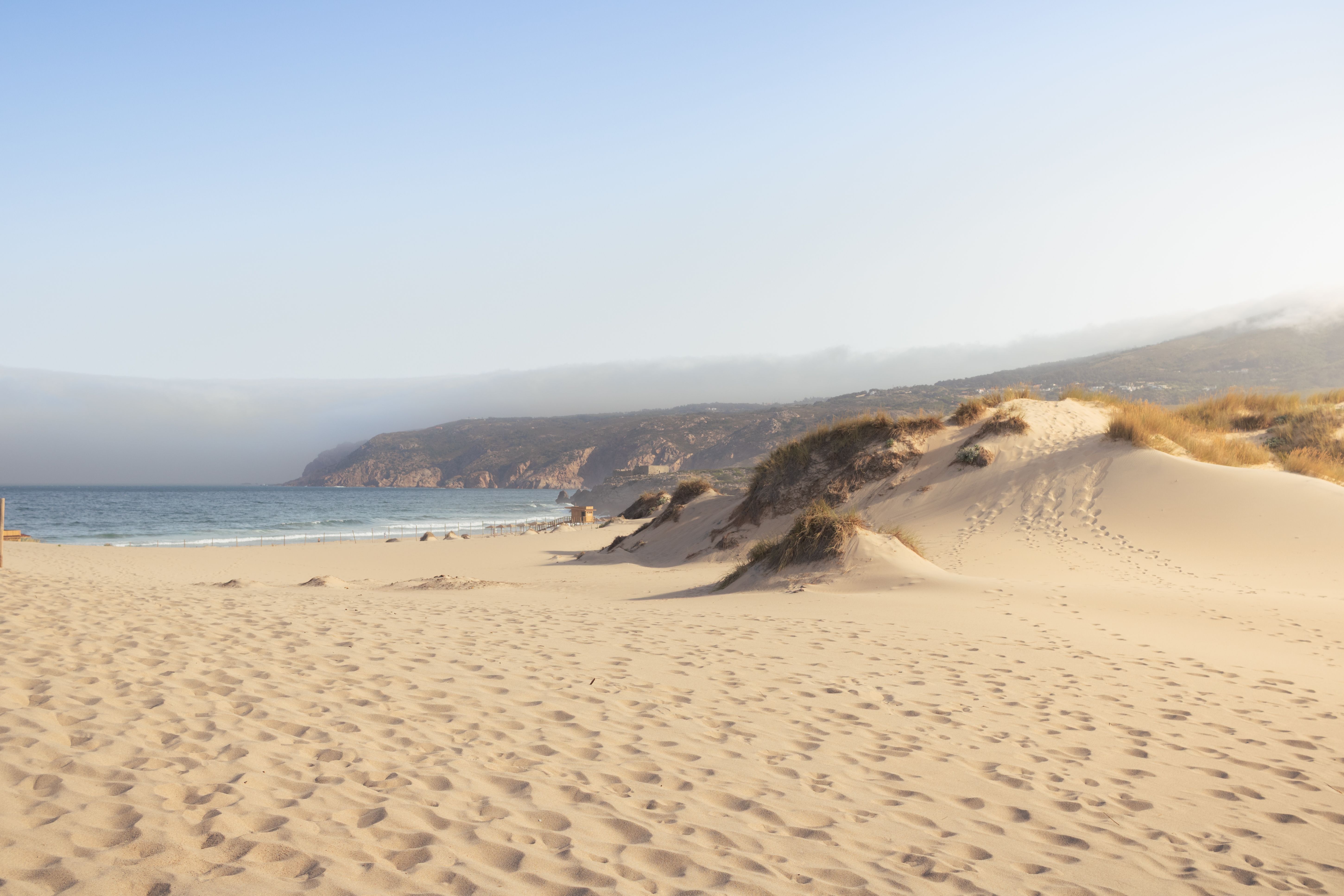 Tranquil sandy dunes meet the ocean at a picturesque beach in Sintra, Lissabon, Portugal.