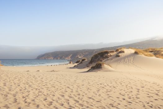 Tranquil sandy dunes meet the ocean at a picturesque beach in Sintra, Lissabon, Portugal.