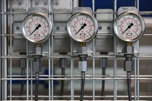 Close-up of industrial pressure gauges mounted on a metal grid in a factory setting.