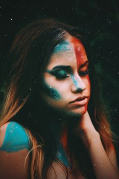 Young tranquil female with ice and flame body art on face leaning on hand with closed eyes on black background