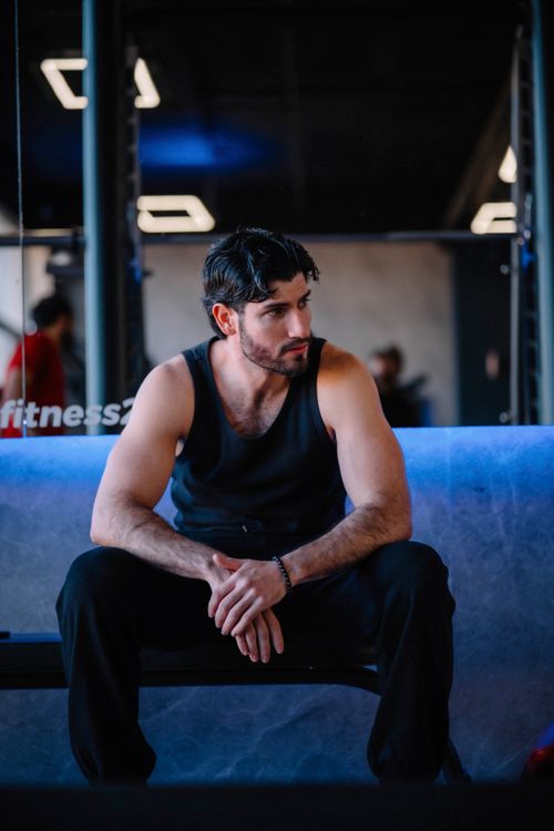 Free Man sitting on bench in gym, wearing black tank top, looking contemplative. Stock Photo