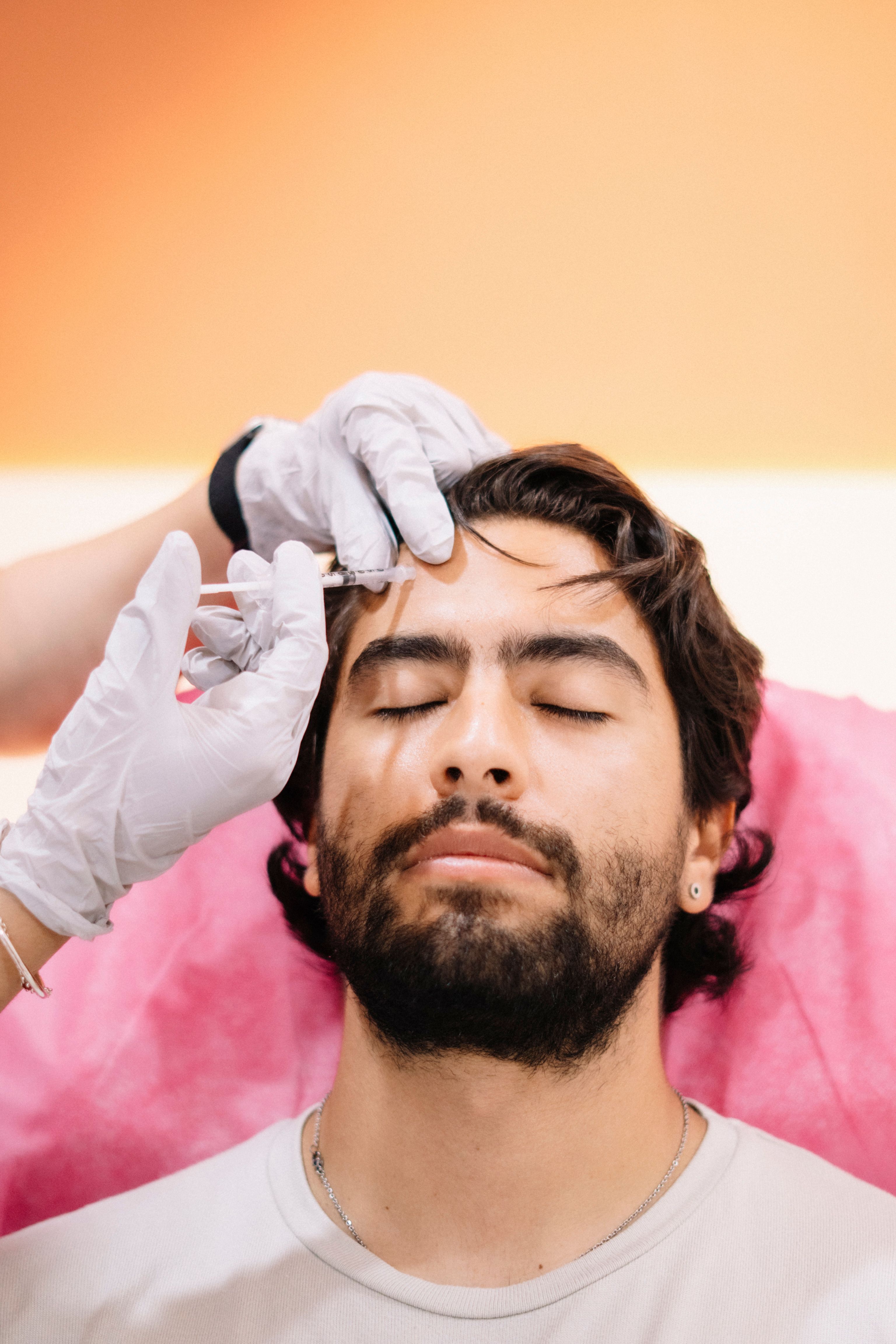 Close-up of a man with eyes closed receiving a botox injection on forehead at a cosmetic clinic.