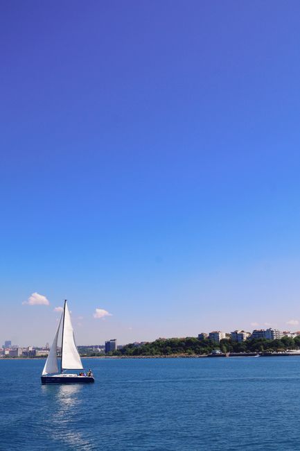 A serene sailboat glides along the Bosphorus near Istanbul, set against a clear blue sky and urban skyline.