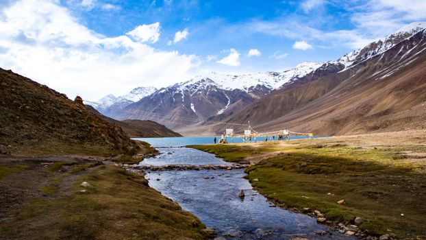 Majestic view of mountains, stream, and lake under a blue sky.