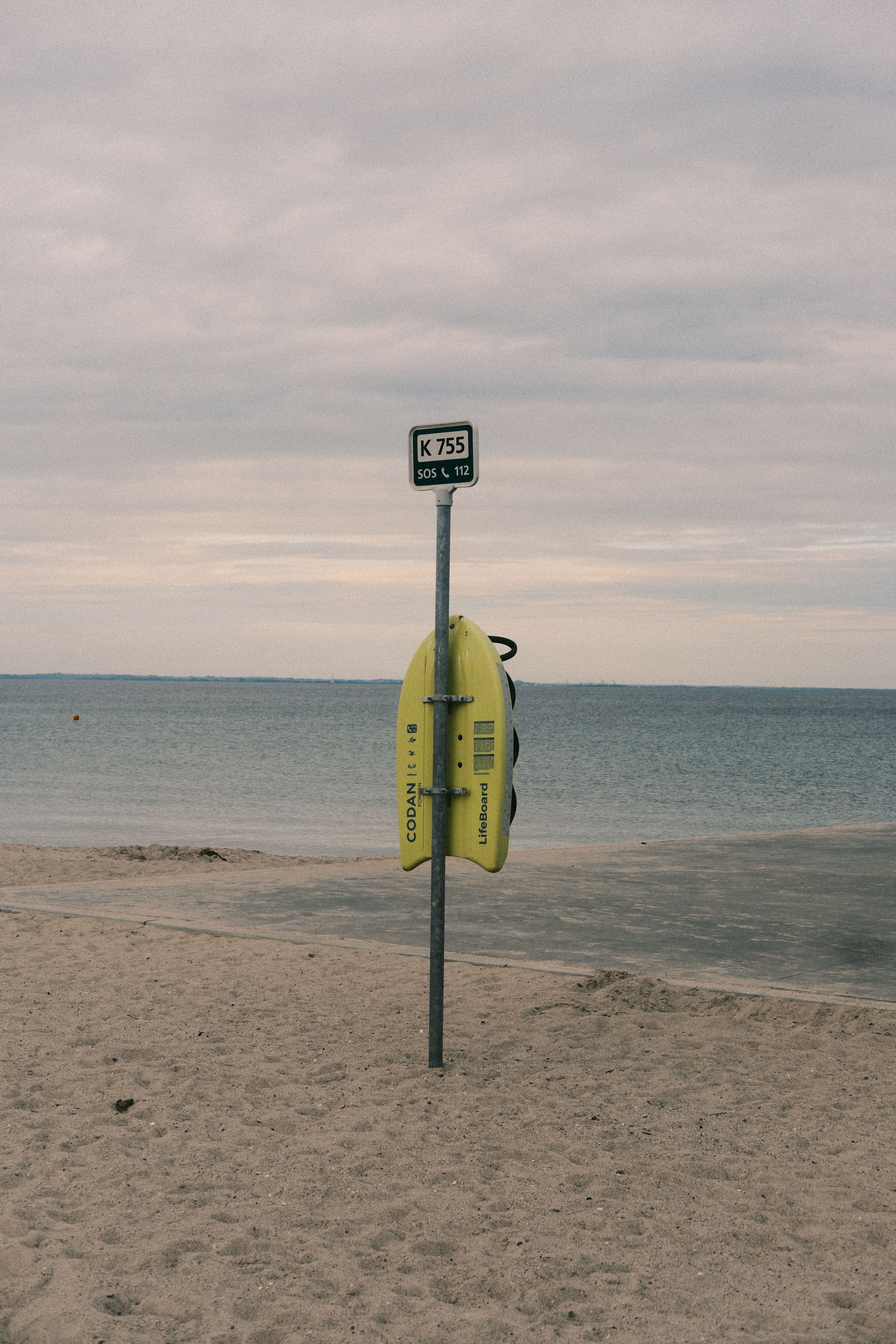 Yellow lifebuoy and signpost at Hellerup Beach in Denmark during a cloudy day.