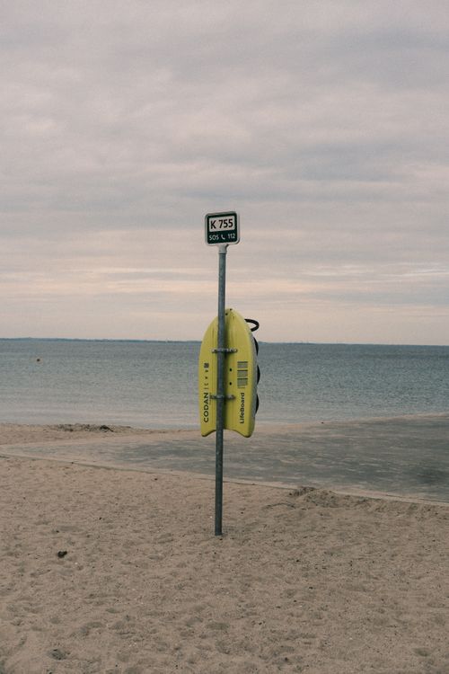 Free Yellow lifebuoy and signpost at Hellerup Beach in Denmark during a cloudy day. Stock Photo