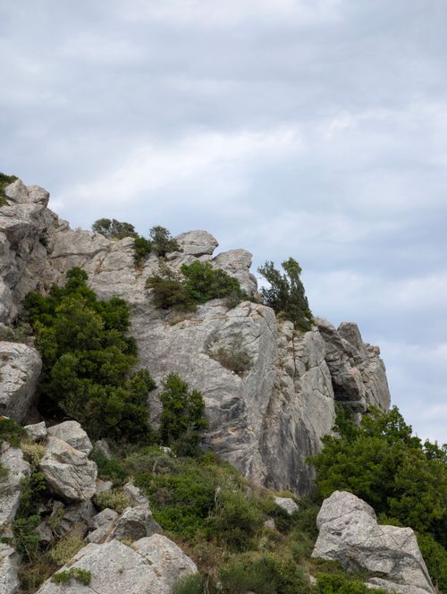Free Majestic rocky cliff with lush green vegetation beneath a cloudy sky, capturing nature's beauty. Stock Photo