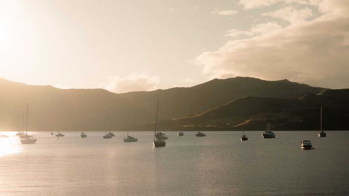 Tranquil view of sailing boats at sunset in Akaroa Harbour, New Zealand, capturing serene beauty.