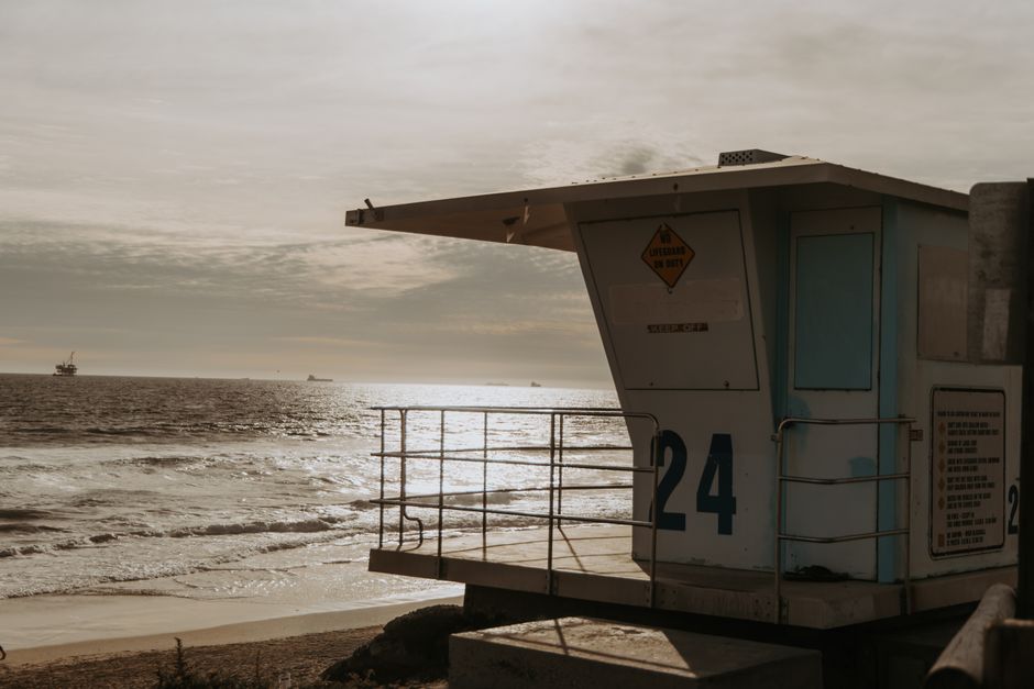 A lifeguard tower stands solitary by the ocean, bathed in sunset light, creating a serene beach scene.