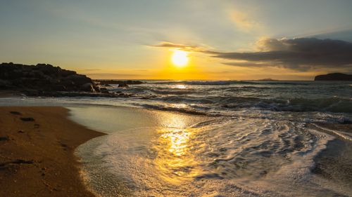 Free Sunset view of ocean waves on a rocky beach shoreline creating a tranquil scene. Stock Photo