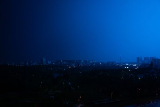 A vibrant cityscape illuminated under the dramatic blue glow of night, featuring silhouetted buildings and streetlights.