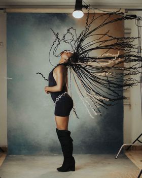 Captivating studio portrait of a woman flipping her braids against a painted backdrop.