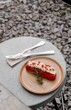 Delicious eclair with cream and pomegranate seeds on outdoor table.