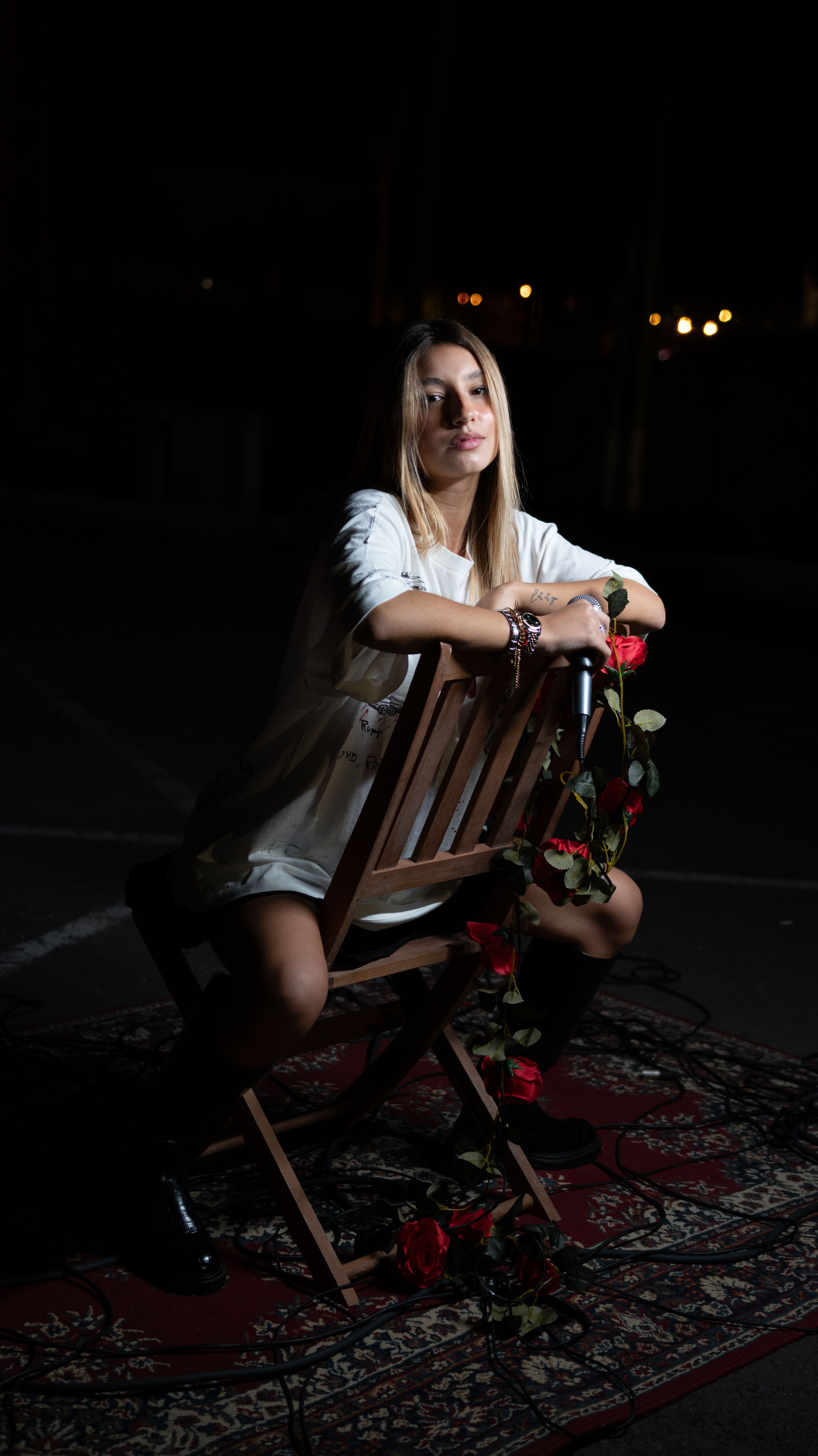 Dramatic night portrait of a woman seated with a microphone and roses.