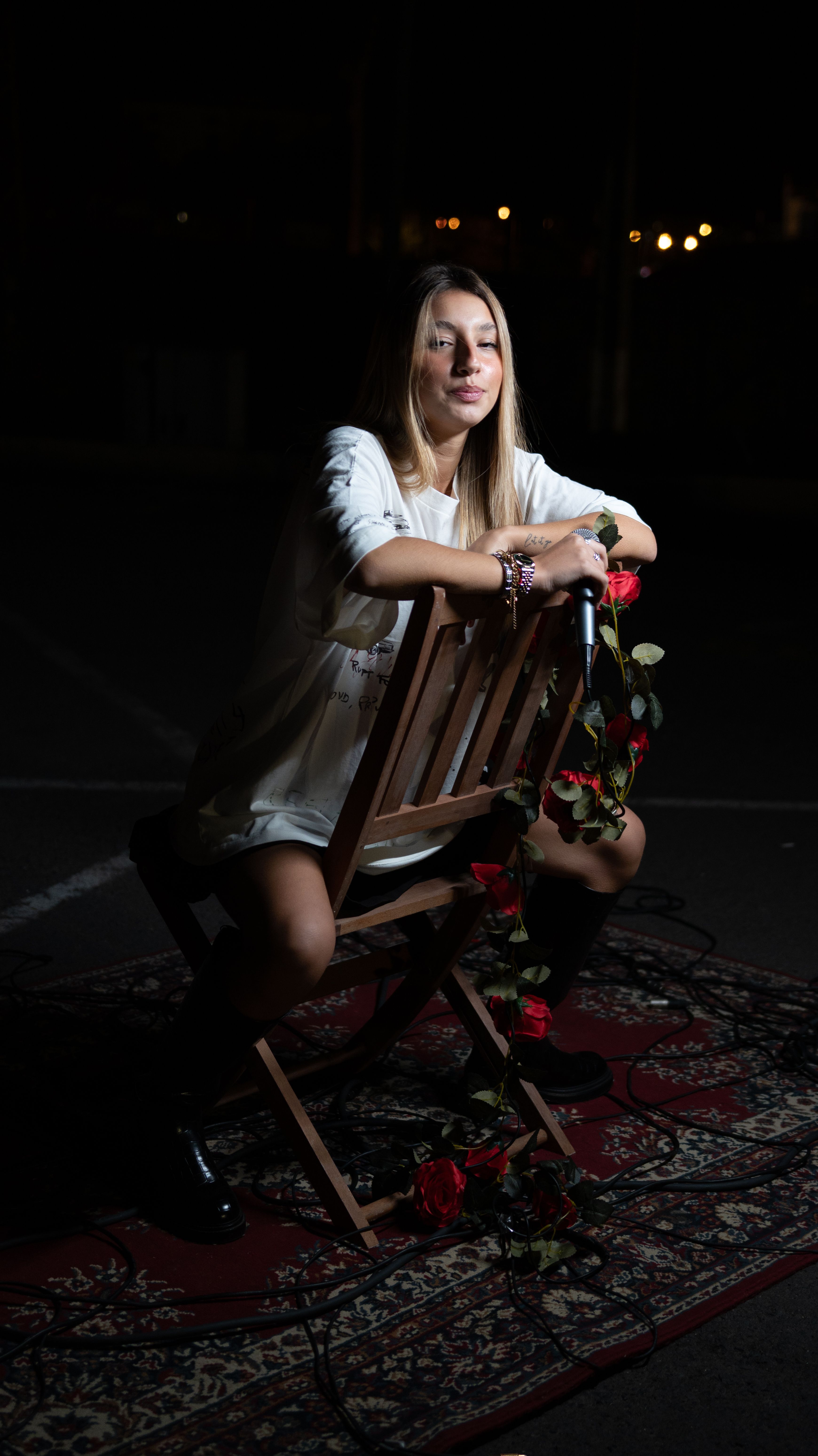 A young woman posing on a chair with roses in a dimly lit studio setting.