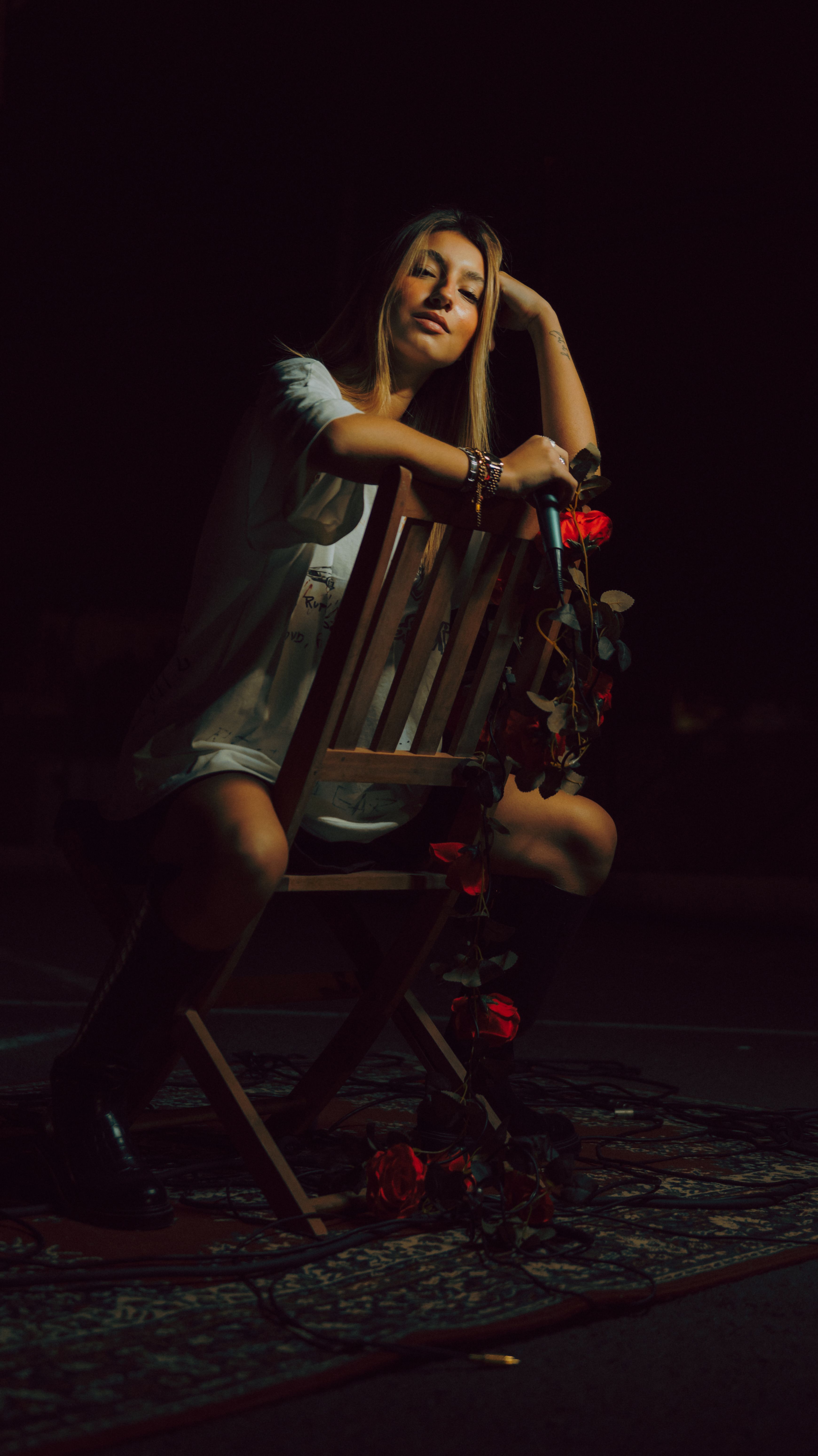 Dramatic portrait of a woman sitting on a chair adorned with roses in low light.