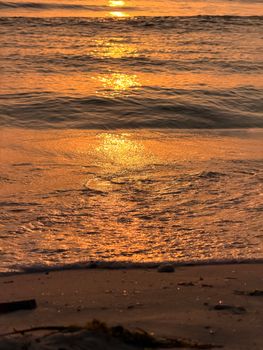 Serene ocean view as the sun sets, casting a golden glow over the gentle waves and sandy beach.