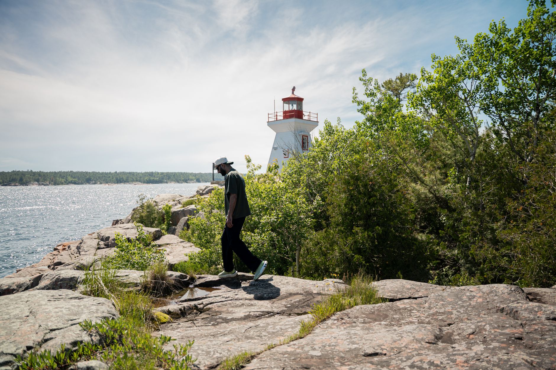 Person walking by a lighthouse on rocky shores in Killarney, Ontario, Canada. Sunny day by the lake.