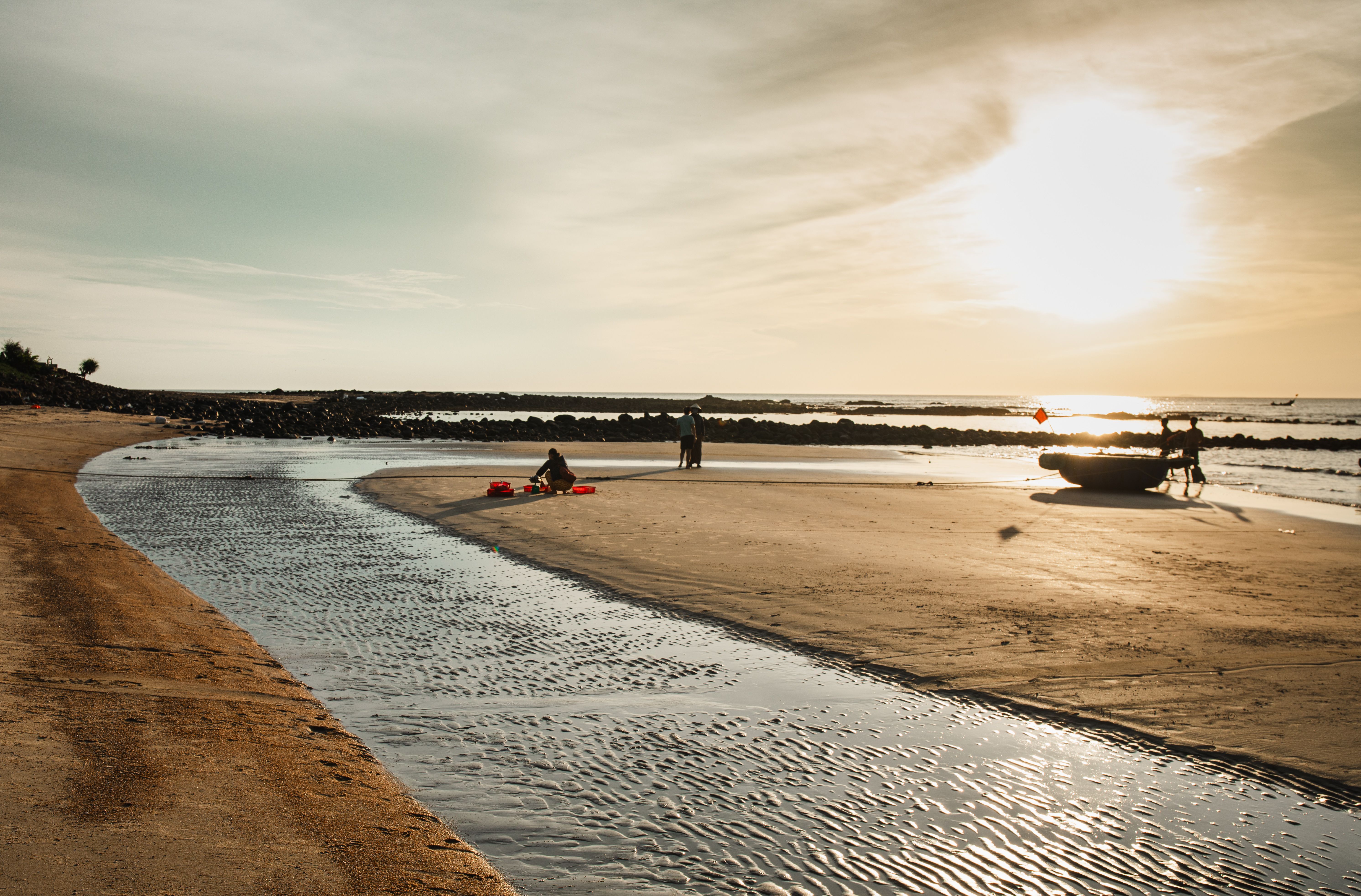 Serene beach scene in Quang Tri, Vietnam at sunset with fishermen and boats.