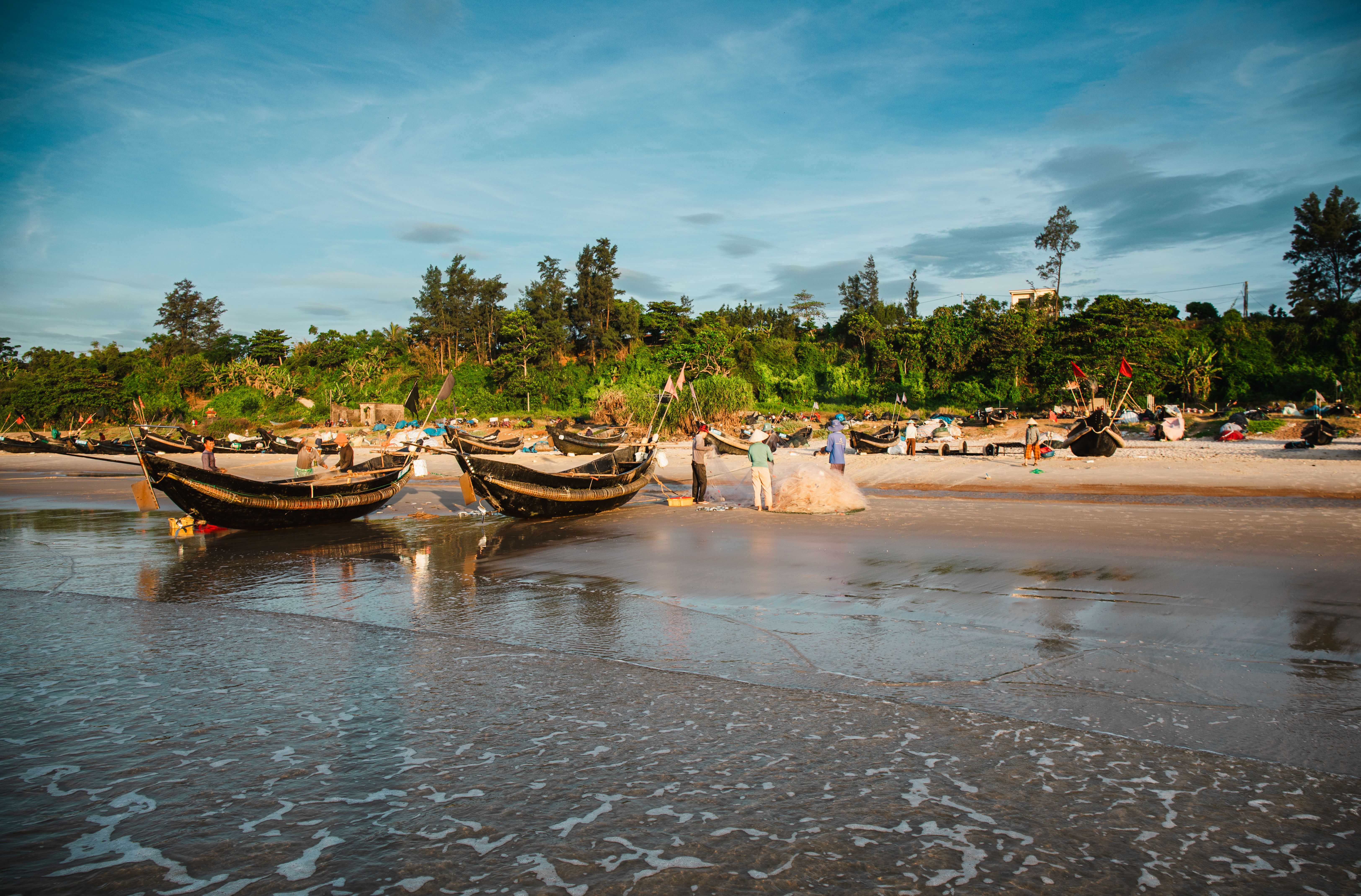 Traditional fishing boats and fishermen on a sunny beach in Quang Tri, Vietnam.